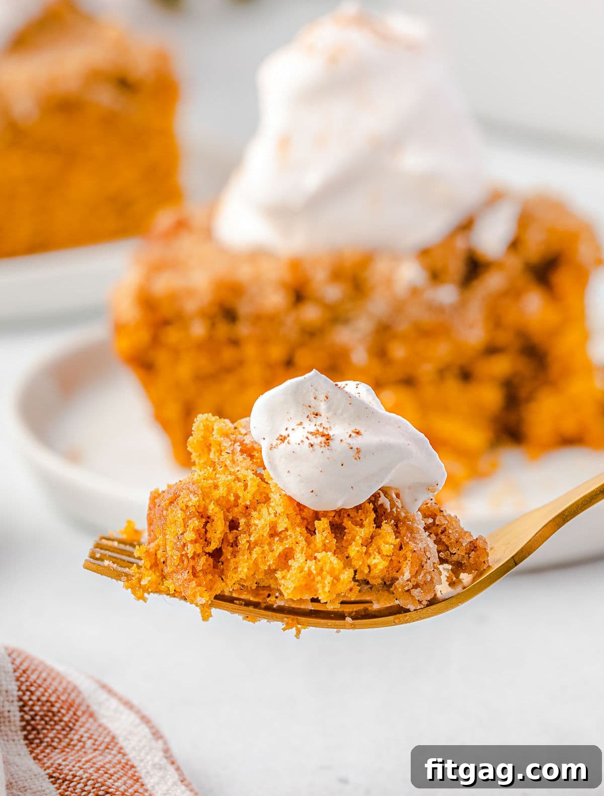 A close-up of a fork taking a bite from a fluffy slice of Pumpkin Coffee Cake, topped with whipped cream, emphasizing the moist texture and inviting flavors of this fall treat.