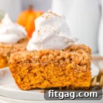 A piece of pumpkin coffee cake sitting on a stack of white plates, topped with whipped cream, enticingly presented as a delicious dessert.
