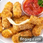 cheese stick with a cheese pull sitting on top of more mozzarella sticks on white plate.