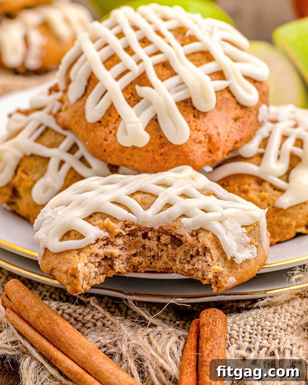 A small white plate holds several apple cookies, each drizzled with maple icing, with one cookie showing a bite taken out of it. The subtle sheen of the icing highlights their freshness.