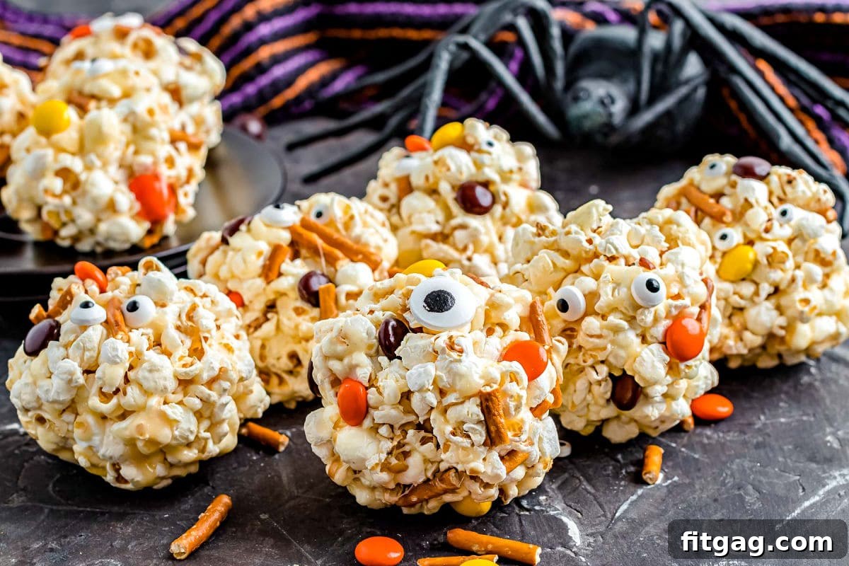 8 popcorn balls with candies and pretzel and candy eyes all ready for Halloween sitting on black surface. 