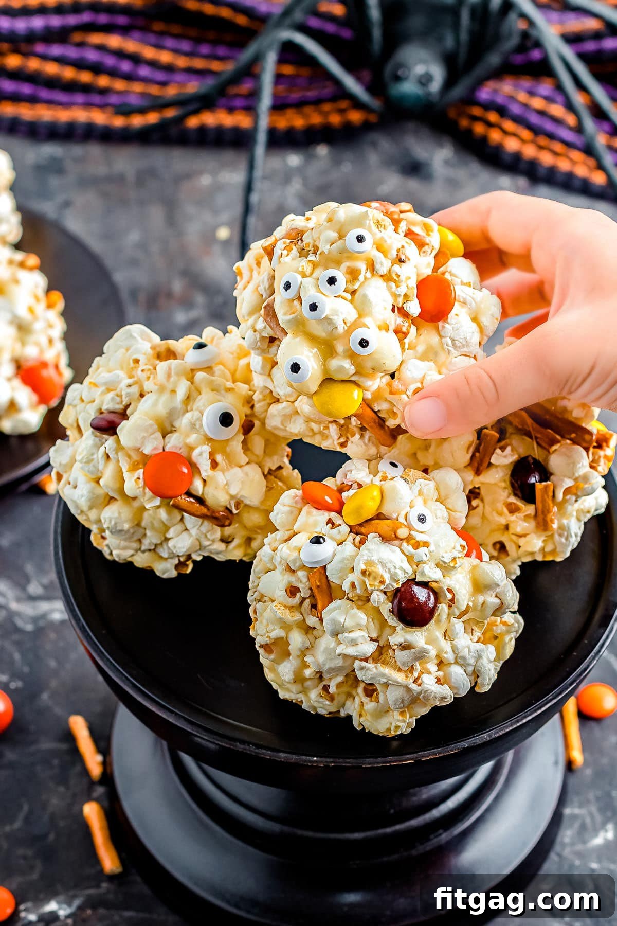 hand picking up a halloween popcorn ball of a tall black cake stand.