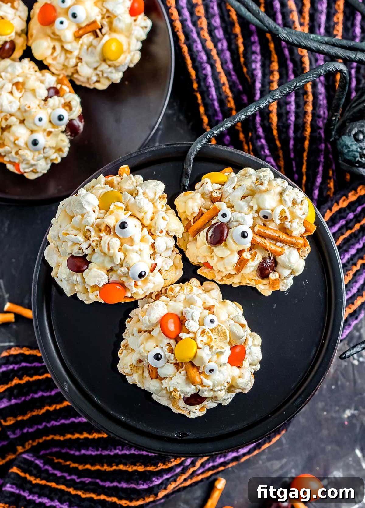 top down look at three popcorn balls on black cake stand that have been decorated with Halloween candy.