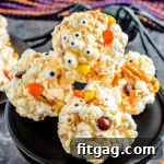 popcorn balls decorated for halloween with pretzels and candies sitting on black cake stand.