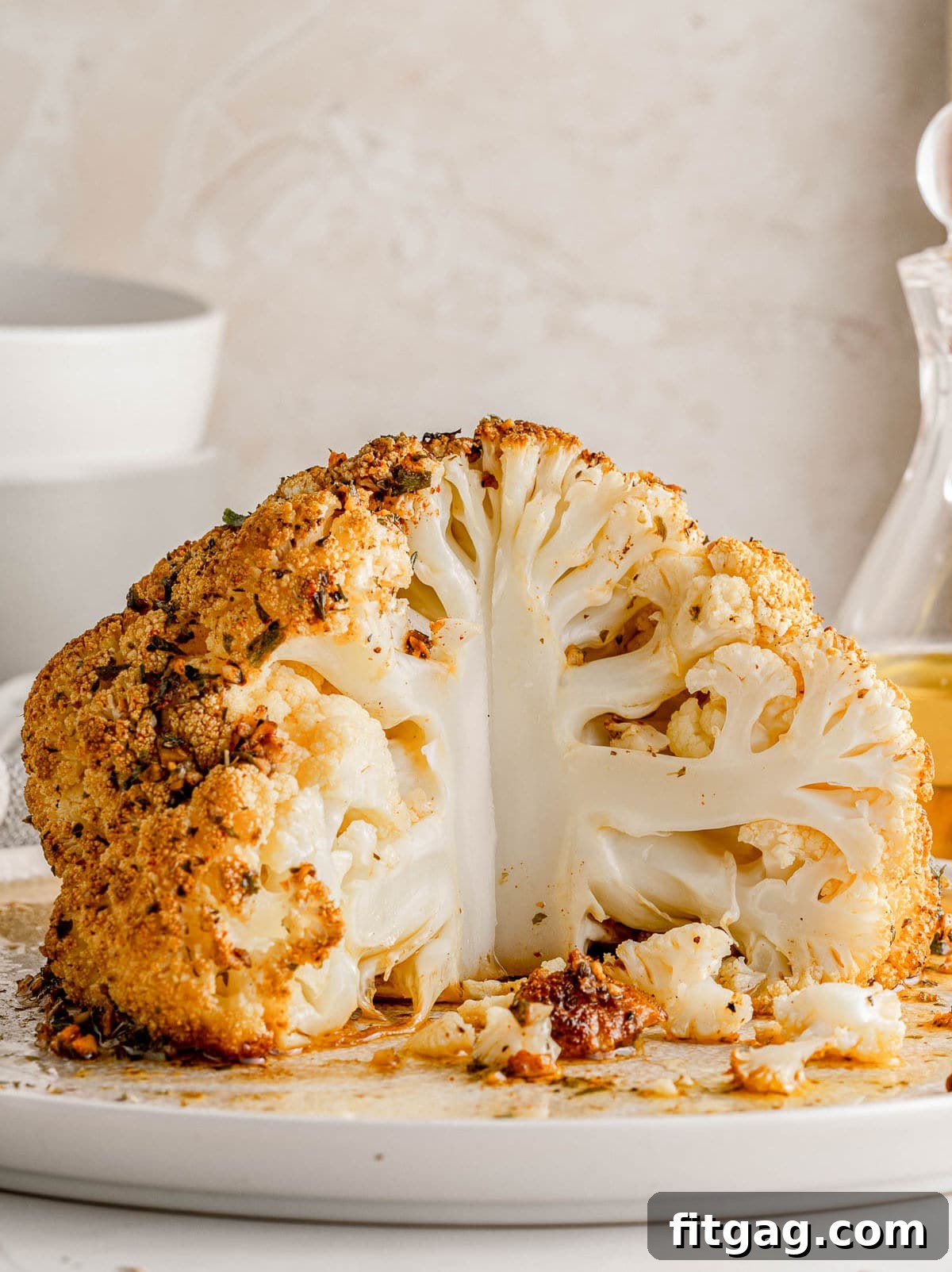 Golden Roasted Cauliflower 2 A beautifully roasted whole cauliflower head, seasoned to perfection and resting on a white plate, with a quarter portion already removed.