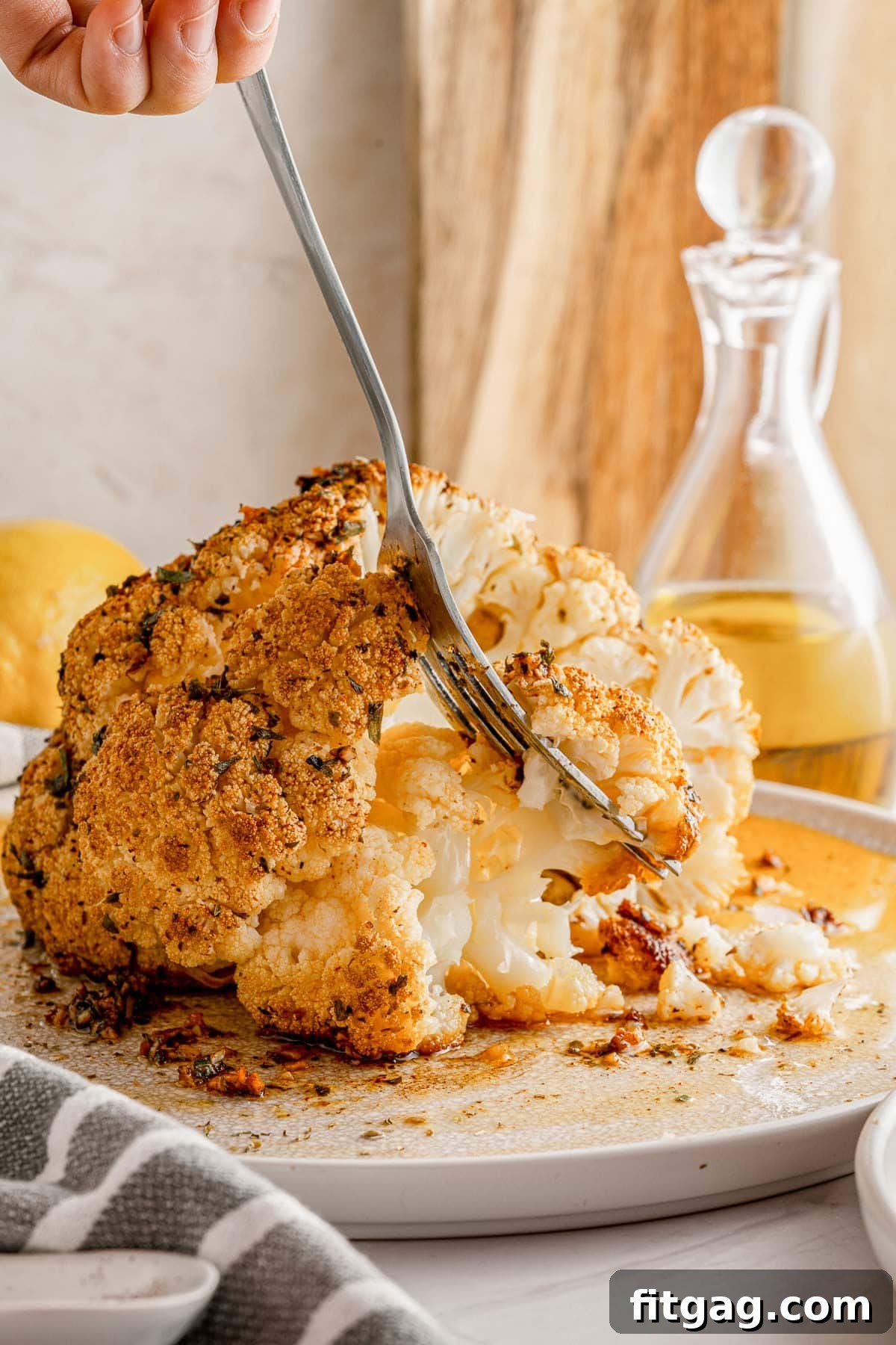 Golden Roasted Cauliflower 5 A fork gently pulls off a tender piece of cauliflower from a beautifully baked whole cauliflower head, showcasing its perfect doneness.