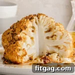 whole cauliflower head that has been seasoned and roasted in oven sitting on white plate with about one quarter of the head removed.