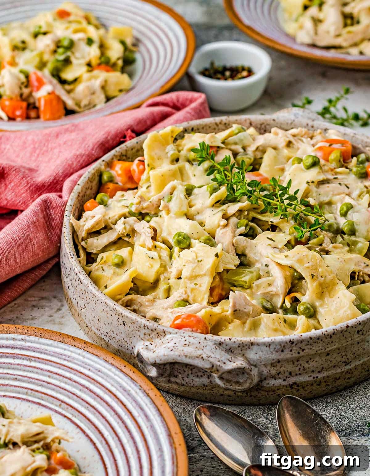 large pottery bowl filled with chicken noodles recipe topped with fresh thyme. Small dinner plates also have servings on them.