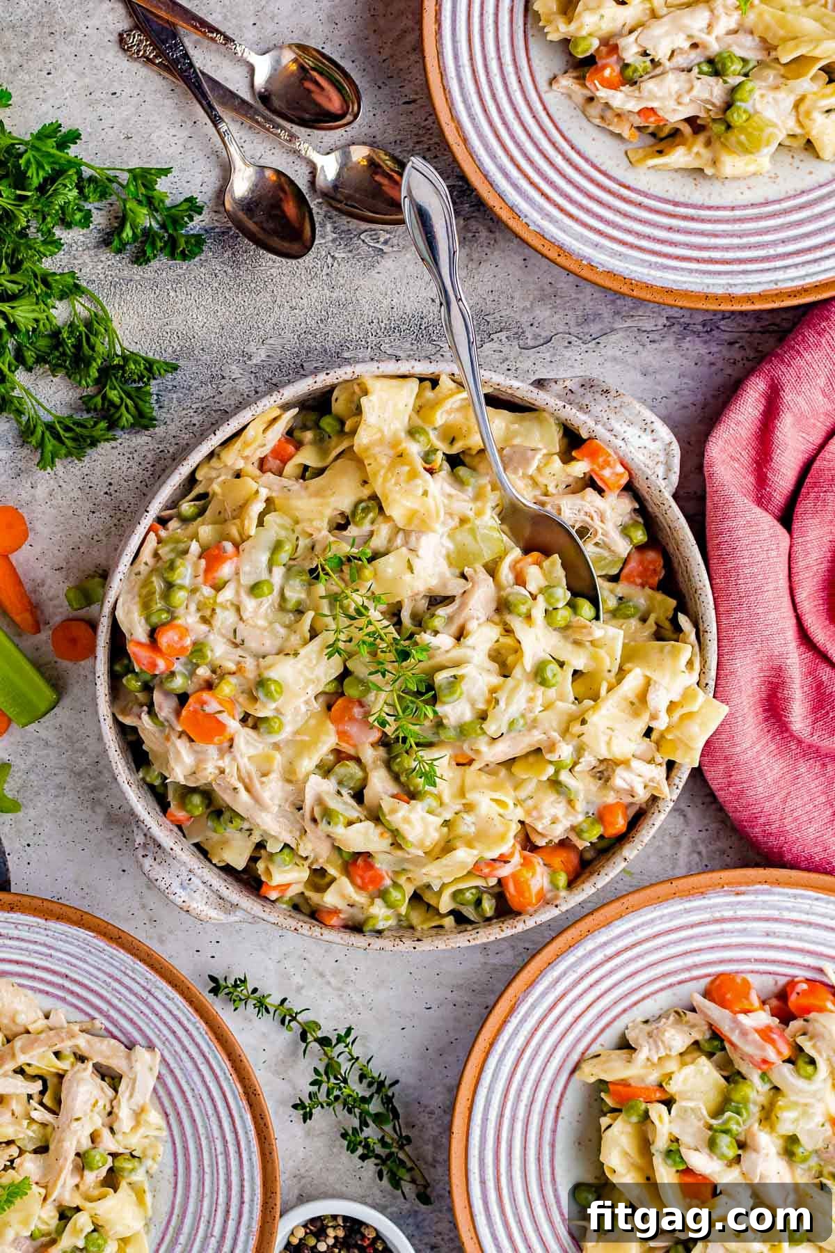 top down view of large serving bowl with chicken noodles recipe and three plates with servings already dished out. 