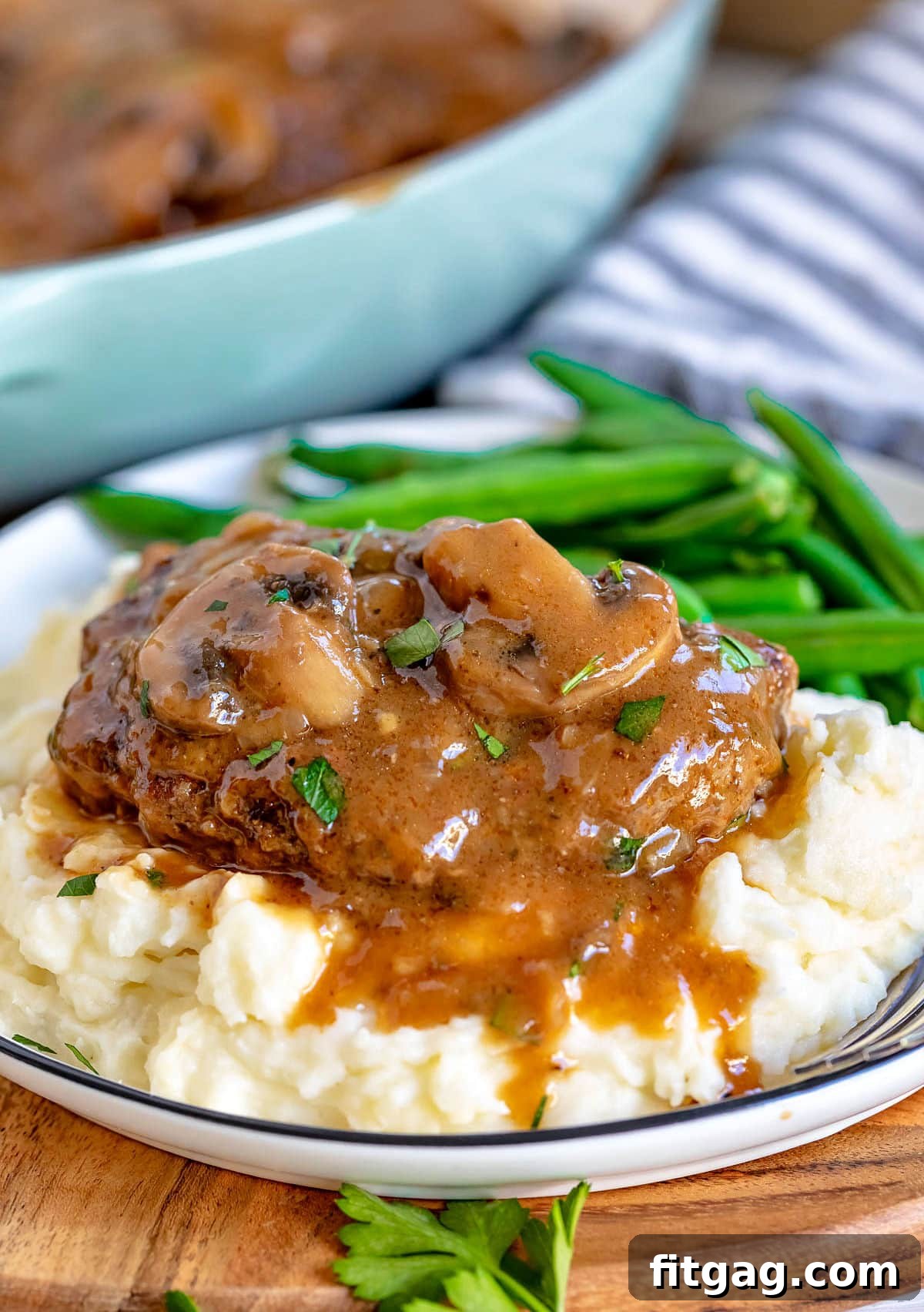 Easy Homestyle Salisbury Steak 3 A serving of Salisbury steak on a bed of fluffy mashed potatoes with green beans, all generously drizzled with mushroom gravy.