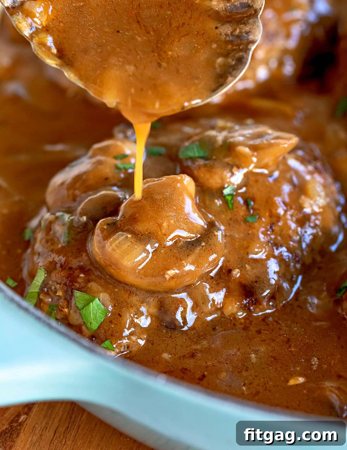 Easy Homestyle Salisbury Steak 6 Rich mushroom gravy being generously poured over a cooked Salisbury steak still in the skillet.