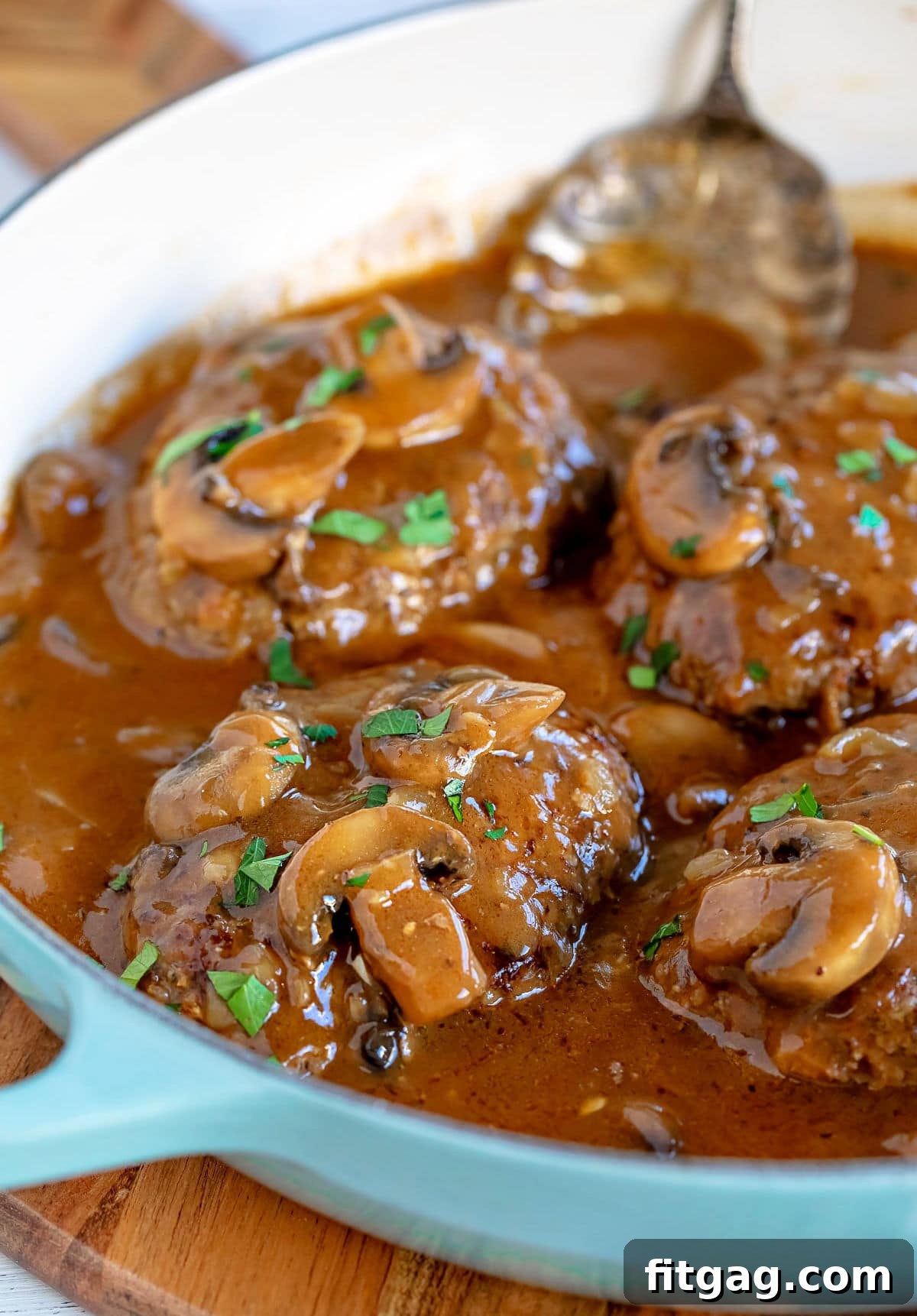 Easy Homestyle Salisbury Steak 7 A large skillet filled with four Salisbury steaks and mushroom gravy, garnished with fresh parsley and an antique spoon in the background.