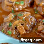 Easy Homestyle Salisbury Steak 8 Four Salisbury steaks in a large skillet with mushroom gravy and fresh parsley sprinkled over the top.