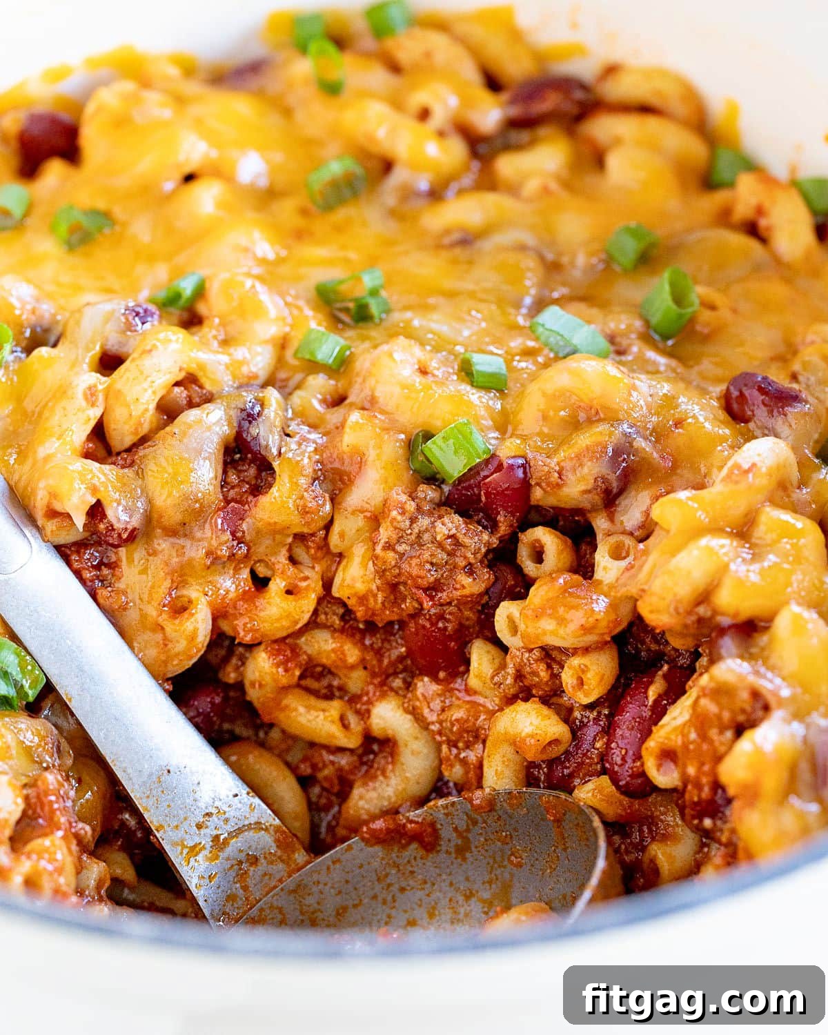 A large scoop of rich chili mac being removed from a pristine white Dutch oven, ready to be served.
