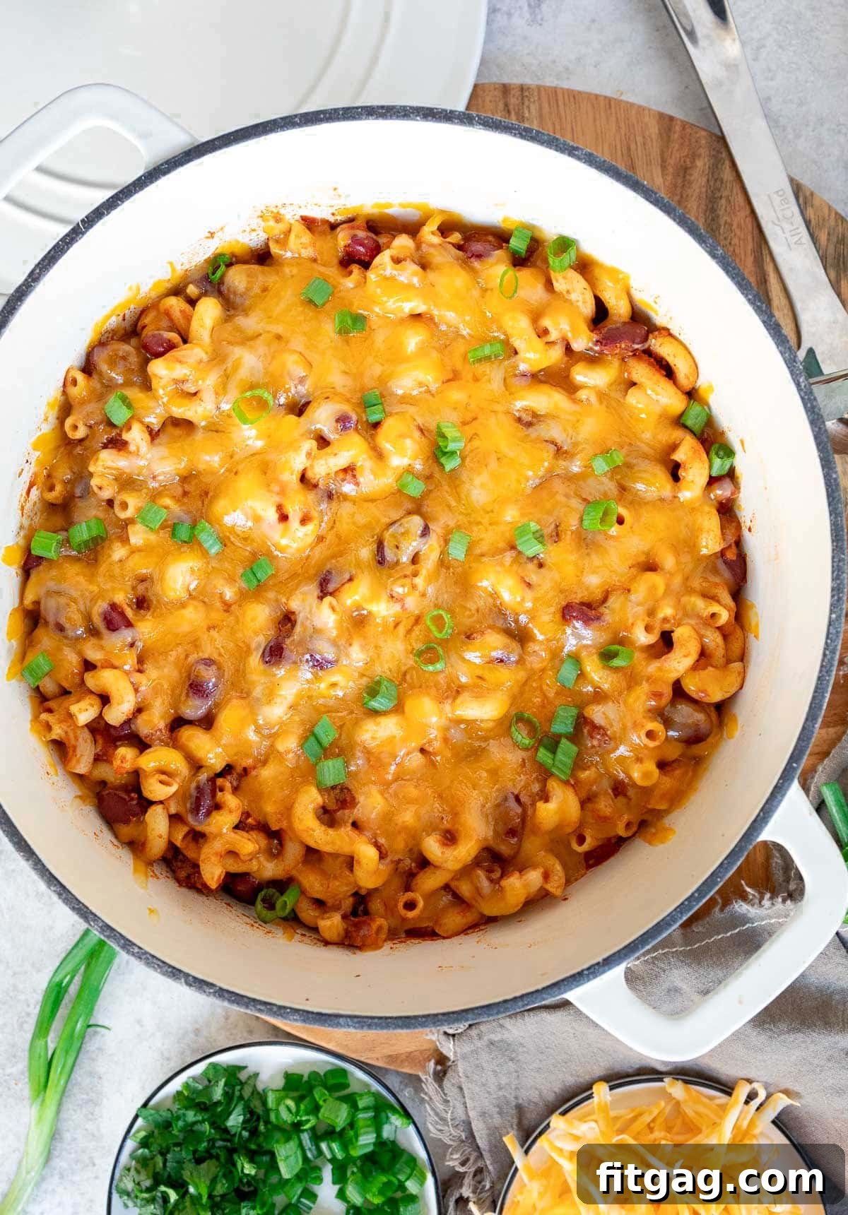 A top-down view of a vibrant chili and macaroni dish nestled in a white Dutch oven, glistening with rich sauce.