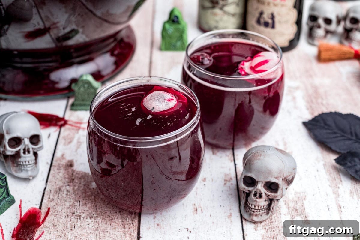 Two glasses filled with dark red Halloween punch, each featuring eerie skull-shaped ice cubes floating on top.