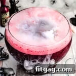 Dark red Halloween punch served in a large glass punch bowl with a mystical fog effect created by dry ice.
