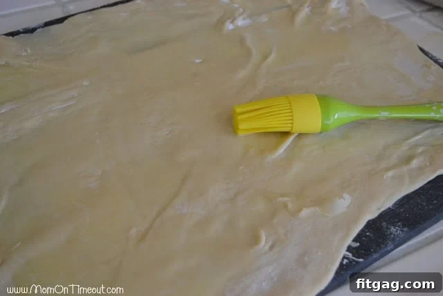 Melted butter spread over a rolled-out rectangle of sticky bun dough, preparing for the filling.