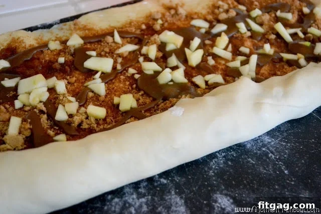 Sticky bun dough being carefully rolled into a tight log, encasing the sweet apple and caramel filling.
