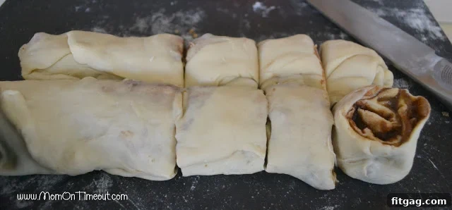 A rolled sticky bun dough log expertly cut into 12 individual spiral buns, ready for baking.