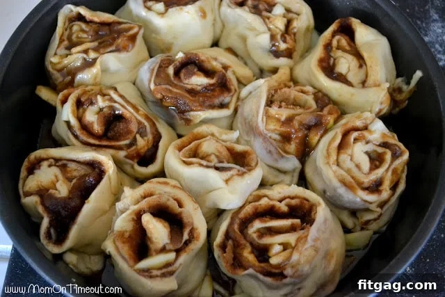 Unbaked sticky buns nestled closely in a round baking pan, ready for their second rise.