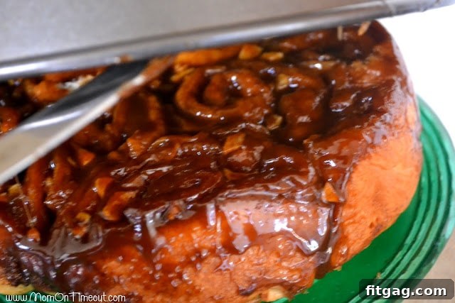 The pan is lifted to reveal perfectly inverted caramel apple sticky buns, dripping with golden caramel.