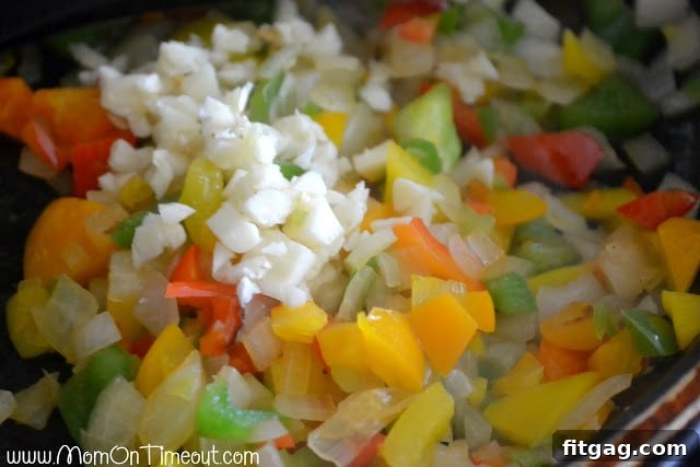 Diced onions and bell peppers sautéing in a pan until soft and translucent, with minced garlic added.