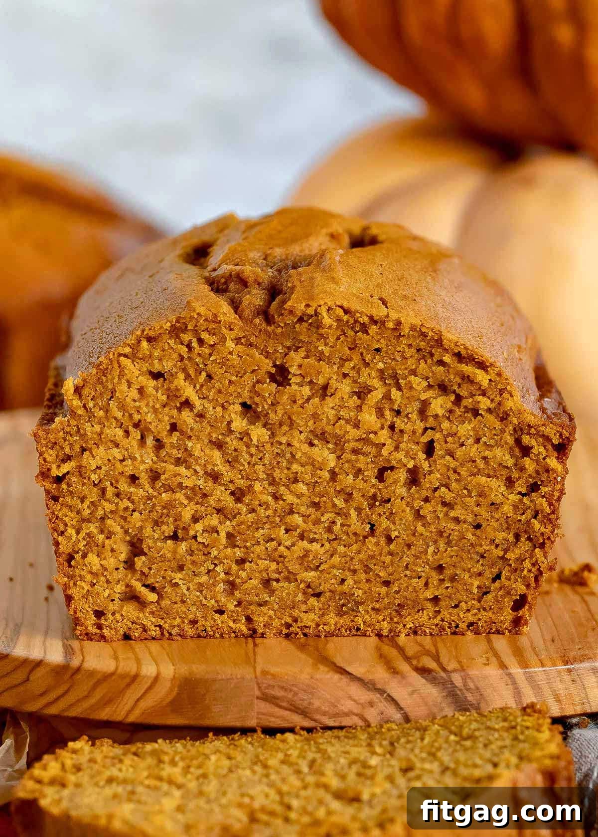 A perfectly baked loaf of moist pumpkin bread resting on an olive wood board, with one generous slice cut and ready to enjoy.