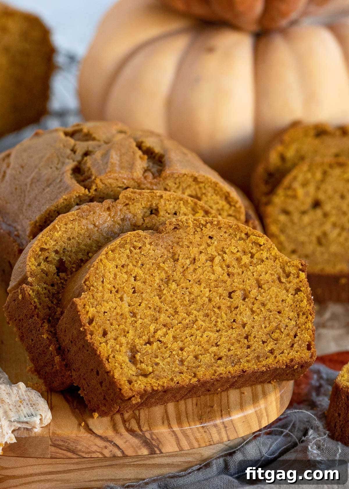 Two enticing slices of pumpkin bread leaning against the remaining loaf on a wooden cutting board.