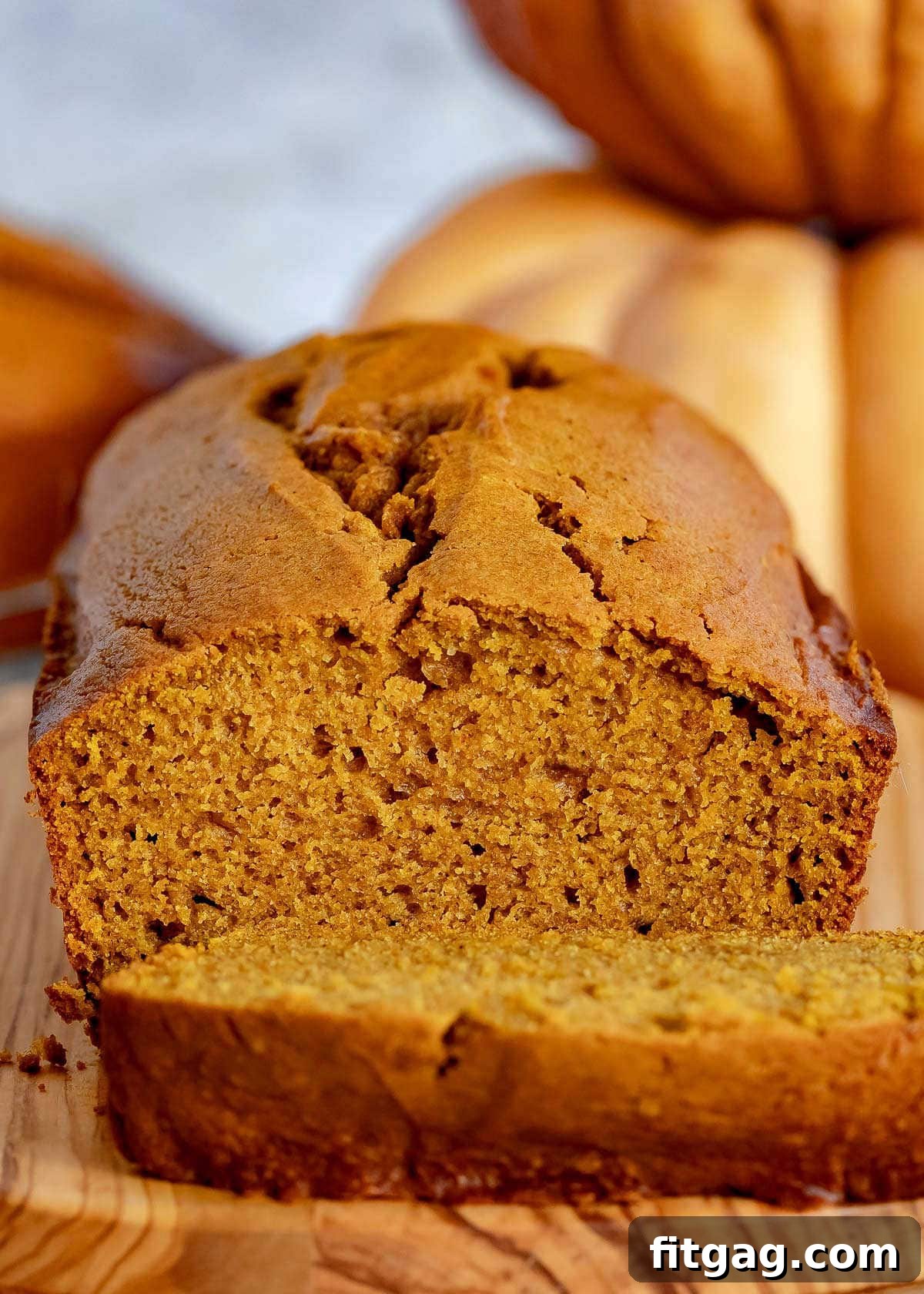 A single loaf of moist pumpkin bread on a rustic wood board, with a piece expertly sliced off, ready for serving.