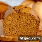 loaf of pumpkin bread sitting on olive board with one piece sliced off.