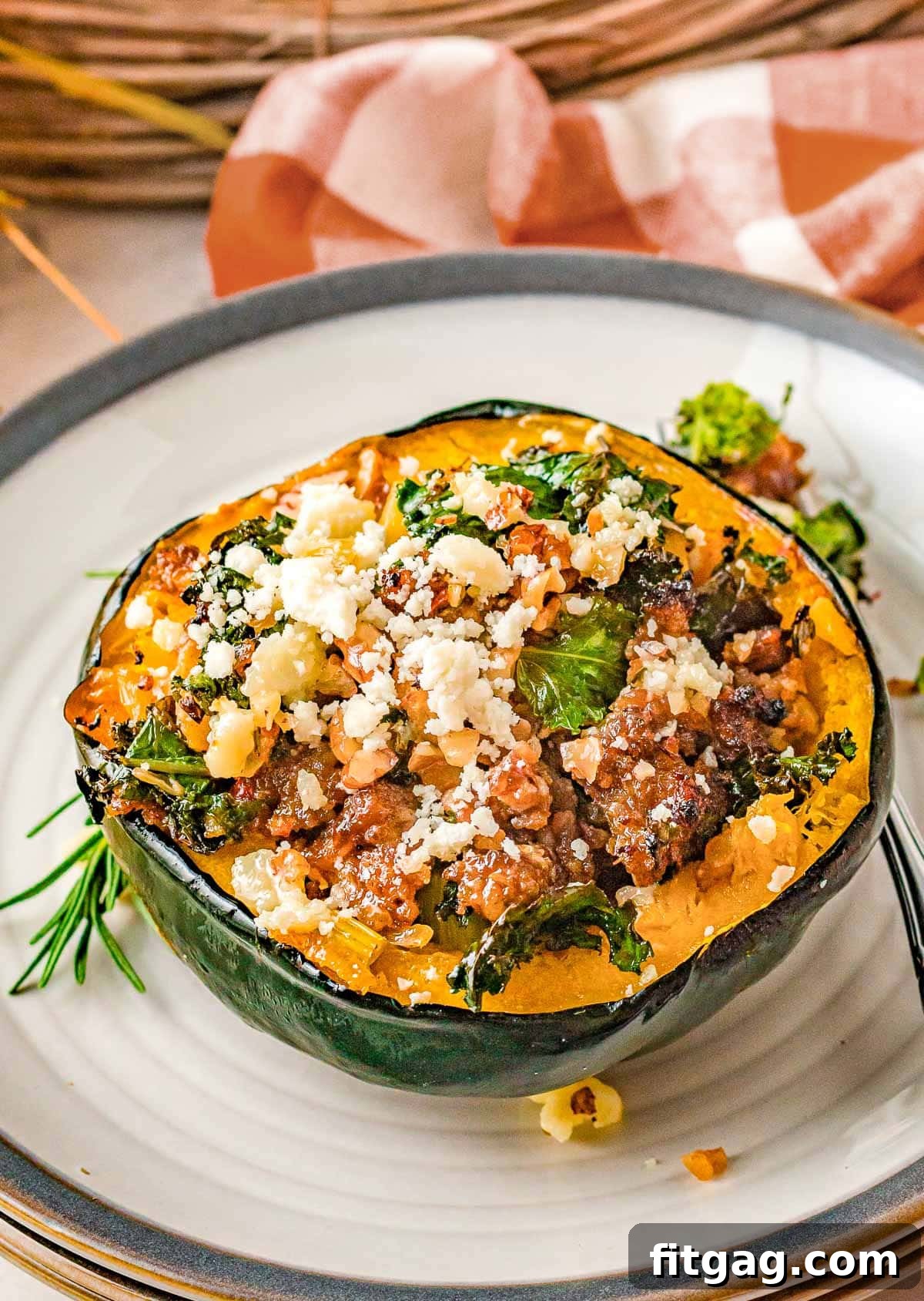 half of an acorn squash stuffed with sausage and veggies sitting on a white plate with a gray rim.