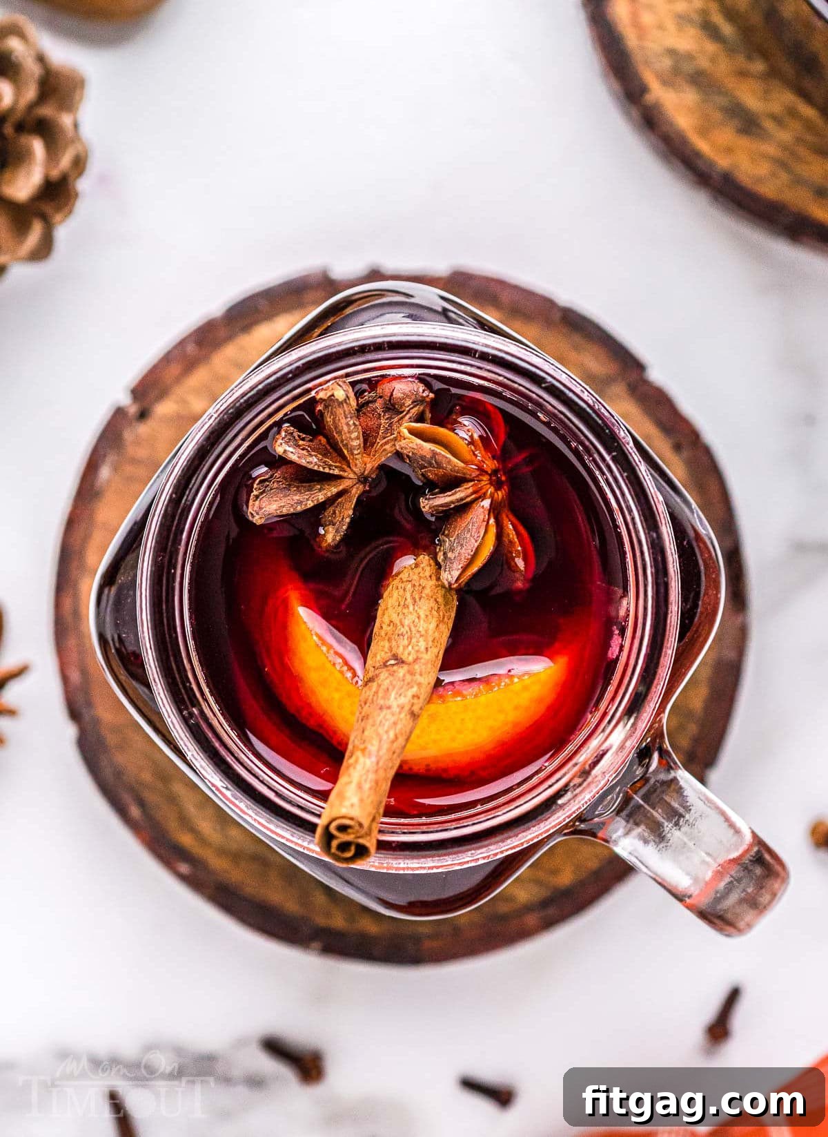 A top-down view into a rustic ball glass jar, brimming with rich mulled wine. It's beautifully garnished with a warm cinnamon stick, a bright orange slice, and a delicate star anise, creating an inviting and festive visual.