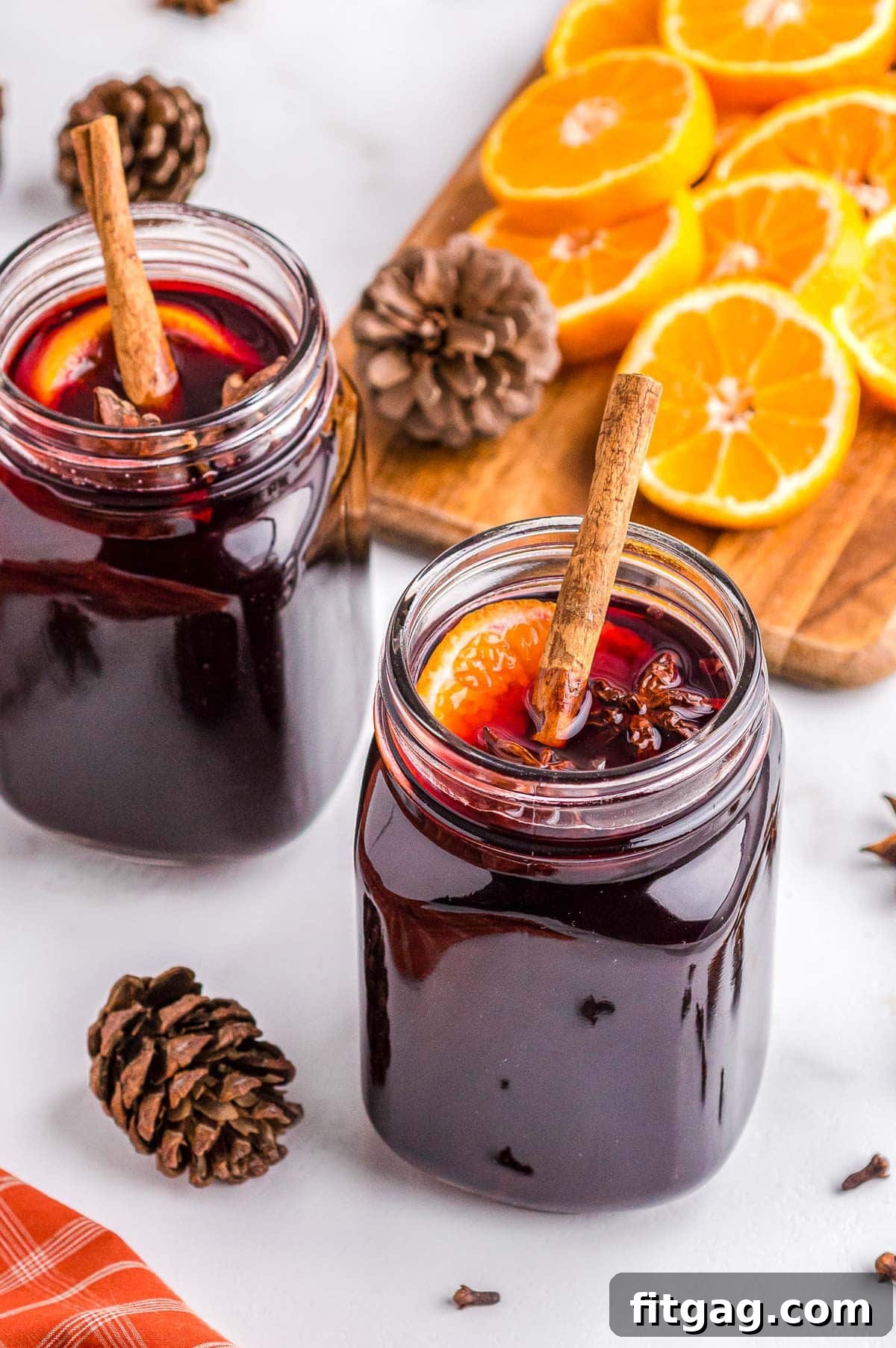 Two large, clear glass mugs brimming with inviting mulled wine, each artfully garnished with aromatic spices and bright orange slices, showcasing a warm and festive presentation.