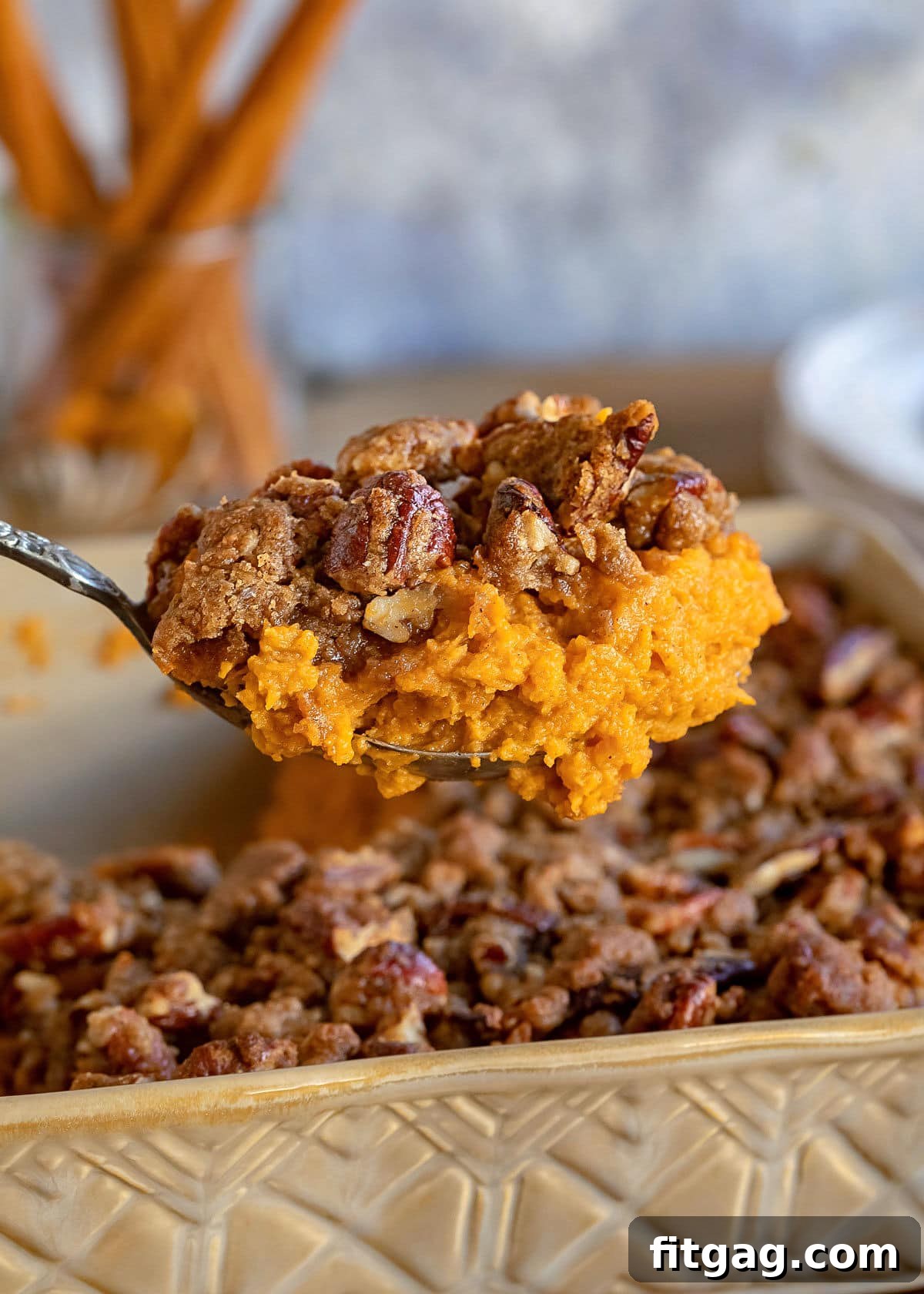 Large scoop of sweet potato casserole being lifted from a baking dish, showcasing its creamy texture and streusel topping.