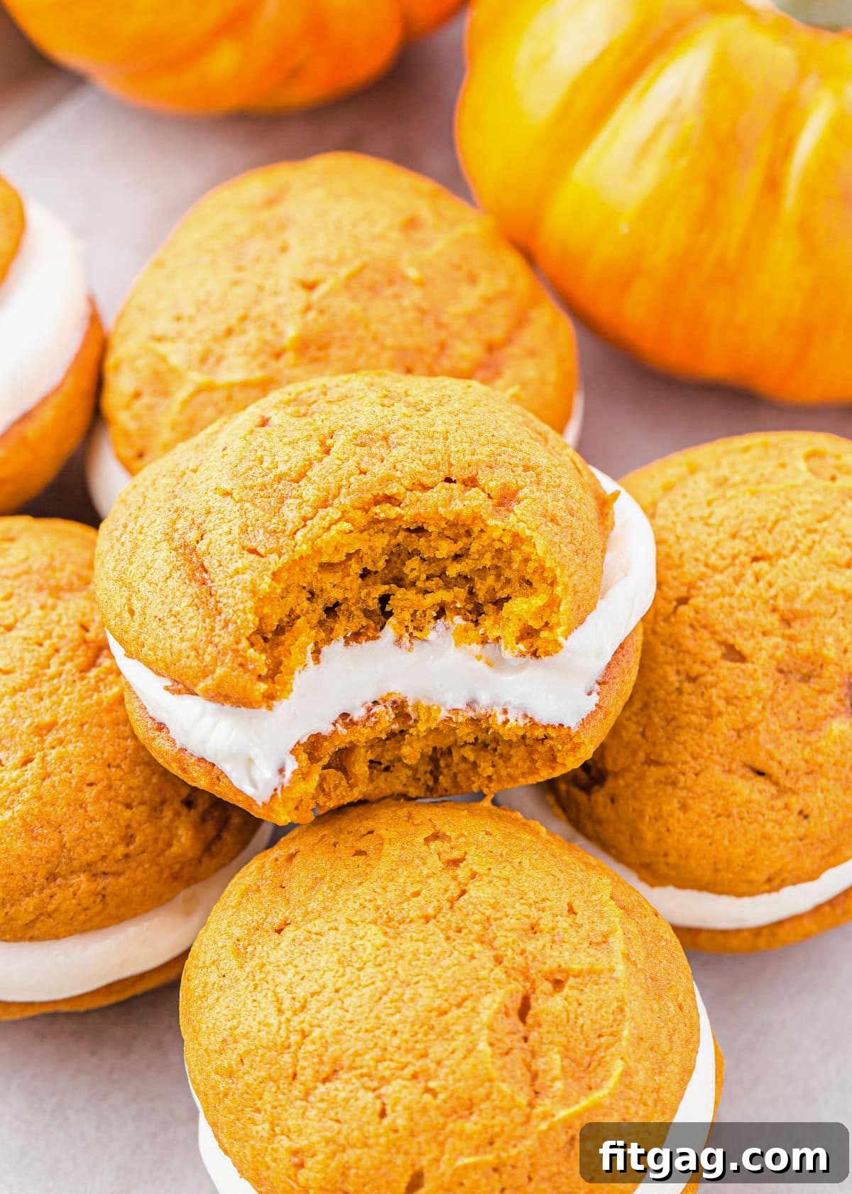 Pillowy Pumpkin Cream Sandwiches 3 pumpkin whoopie pie with bite taken out of it sitting with more whoopie pies.