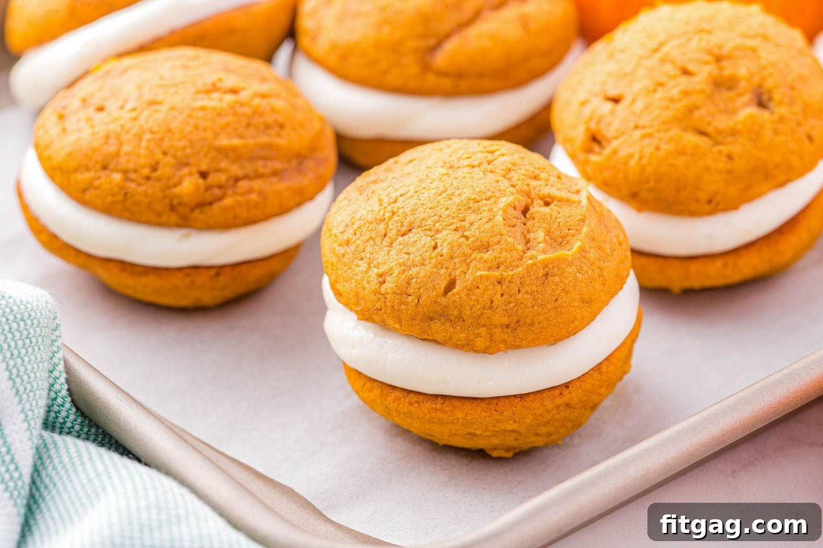 Pillowy Pumpkin Cream Sandwiches 7 whoopie pies assembled and sitting on a baking sheet on top of a piece of parchment paper.