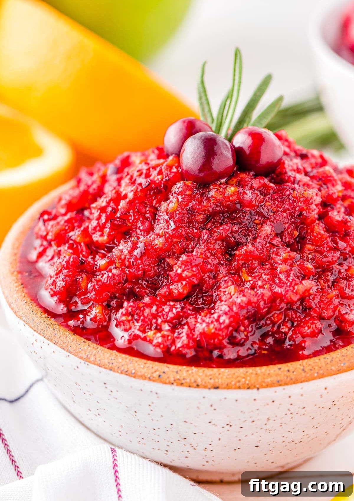 A small white bowl filled with vibrant cranberry orange relish, garnished with fresh rosemary and whole cranberries, ready to serve for a festive holiday meal.