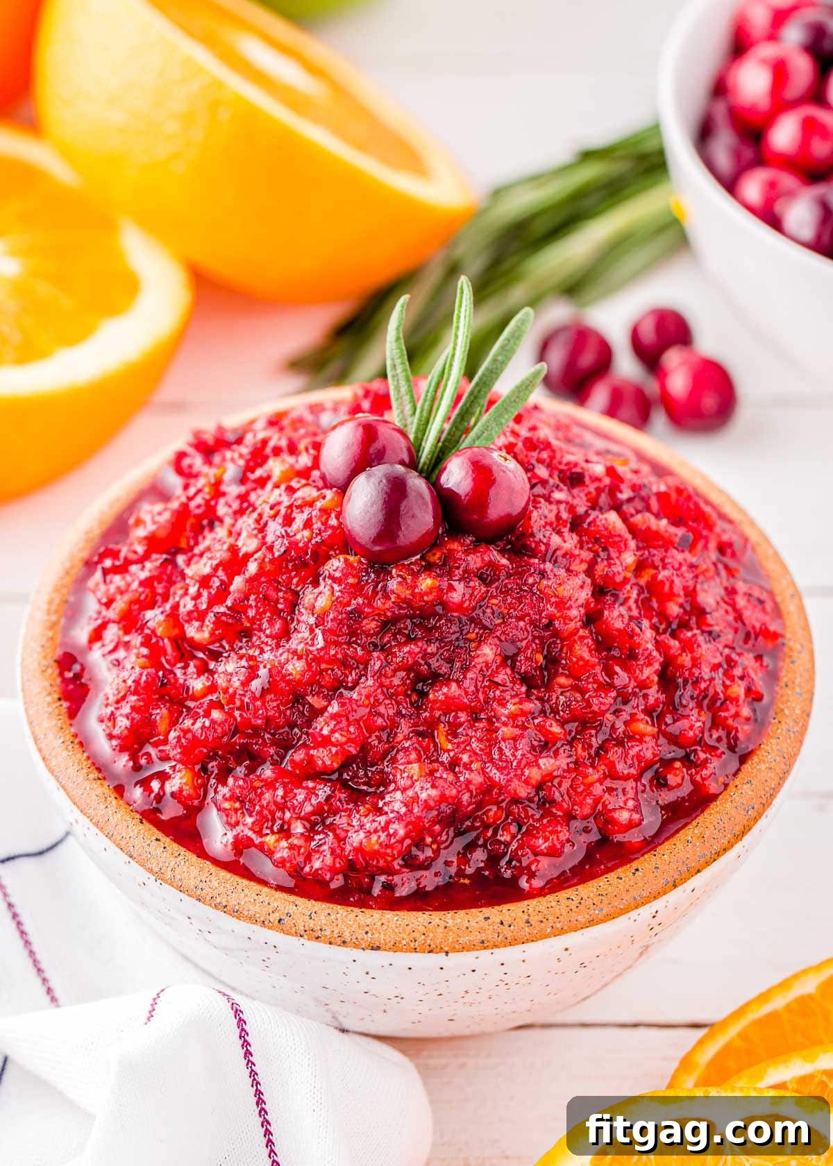A beautiful bowl of bright, ruby-red cranberry orange relish, elegantly topped with a sprig of fresh rosemary and three whole cranberries, ready for serving.