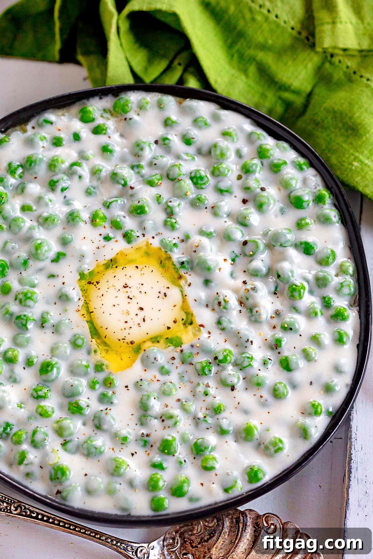 Velvet Peas 3 Top-down view of creamed peas in a black bowl, garnished with melted butter and freshly cracked black pepper.