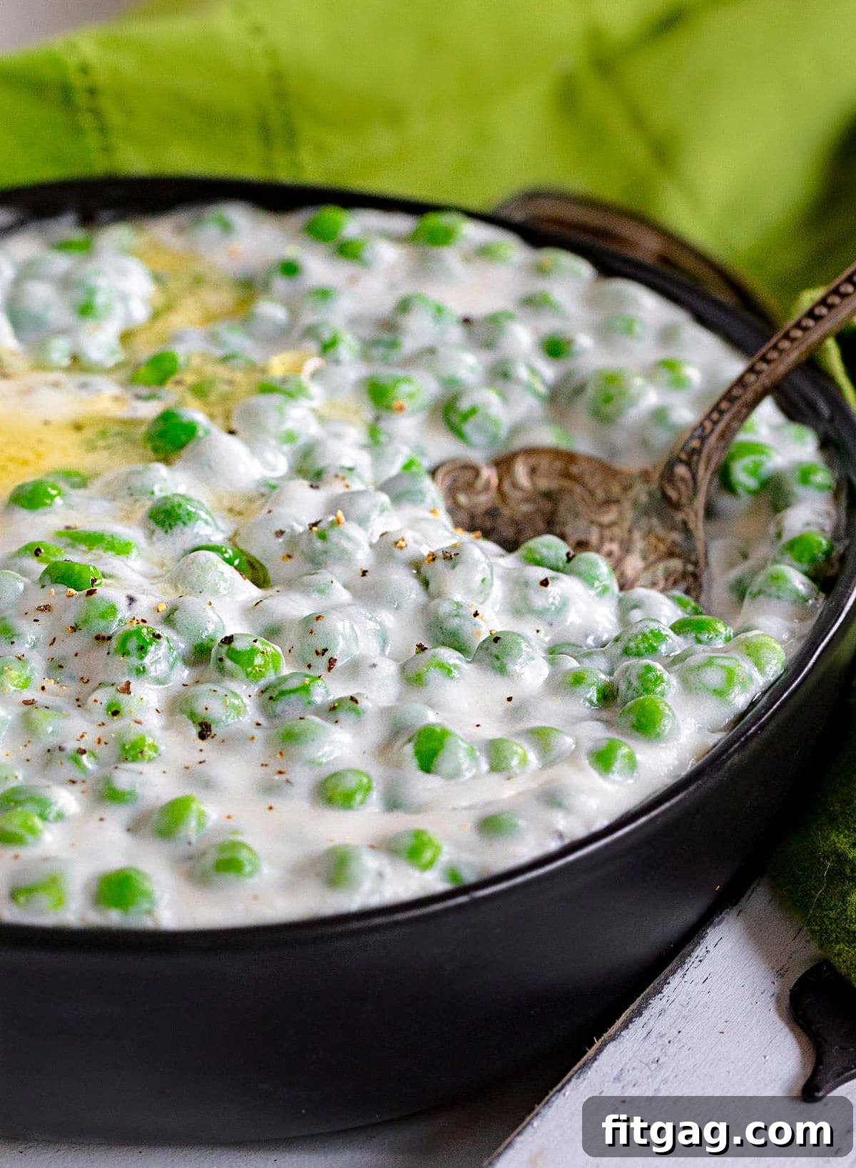 Velvet Peas 6 Creamed peas served in a shallow black bowl, adorned with melted butter and an antique serving spoon. A green napkin is in the background.