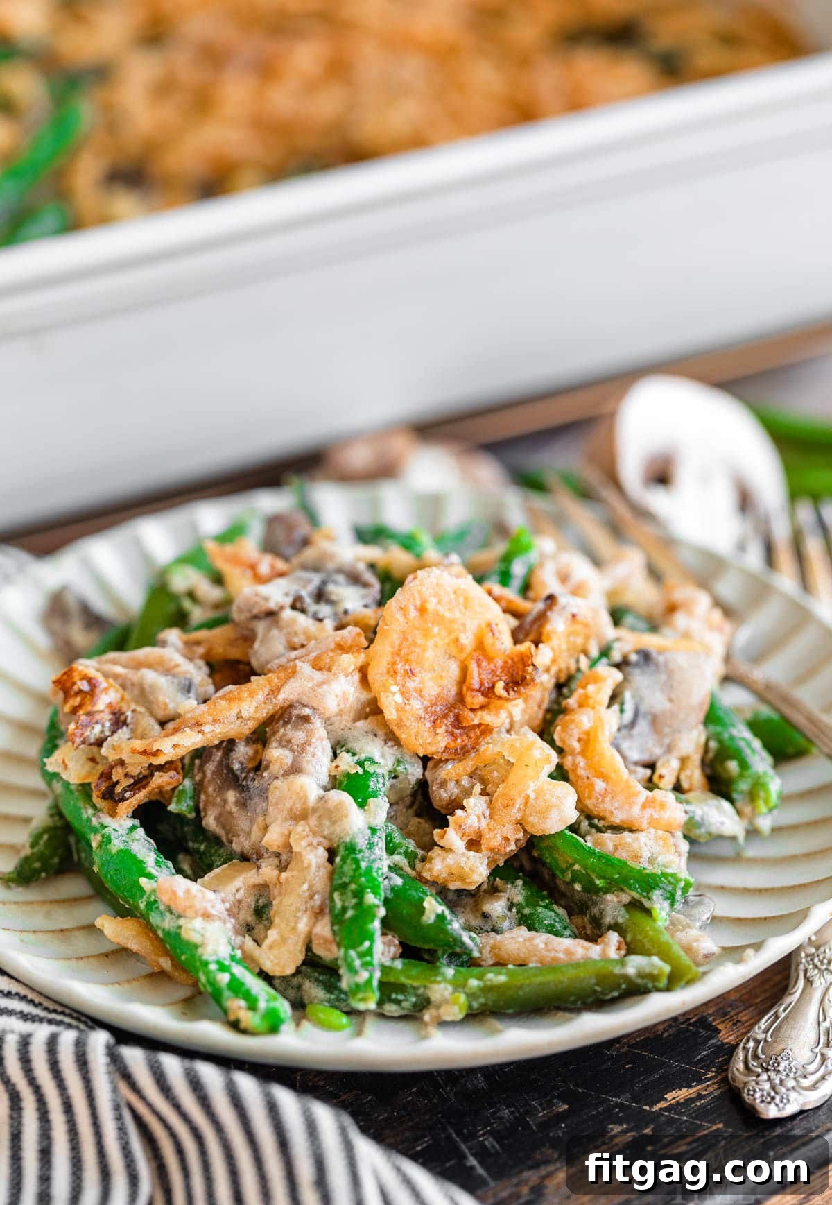 Crispy Onion Green Bean Delight 6 A small plate holds a single serving of green bean casserole, perfectly portioned, with the larger casserole dish visible in the softened background.