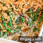 green bean casserole in a large white baking dish topped with fried onions. two silver serving spoons are in the dish with a serving or two removed.