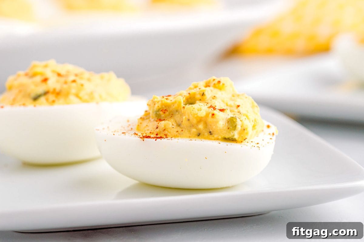 Two perfectly prepared deviled eggs sit side by side on a pristine white plate, showcasing their creamy filling and delicate paprika dusting from a close side profile.