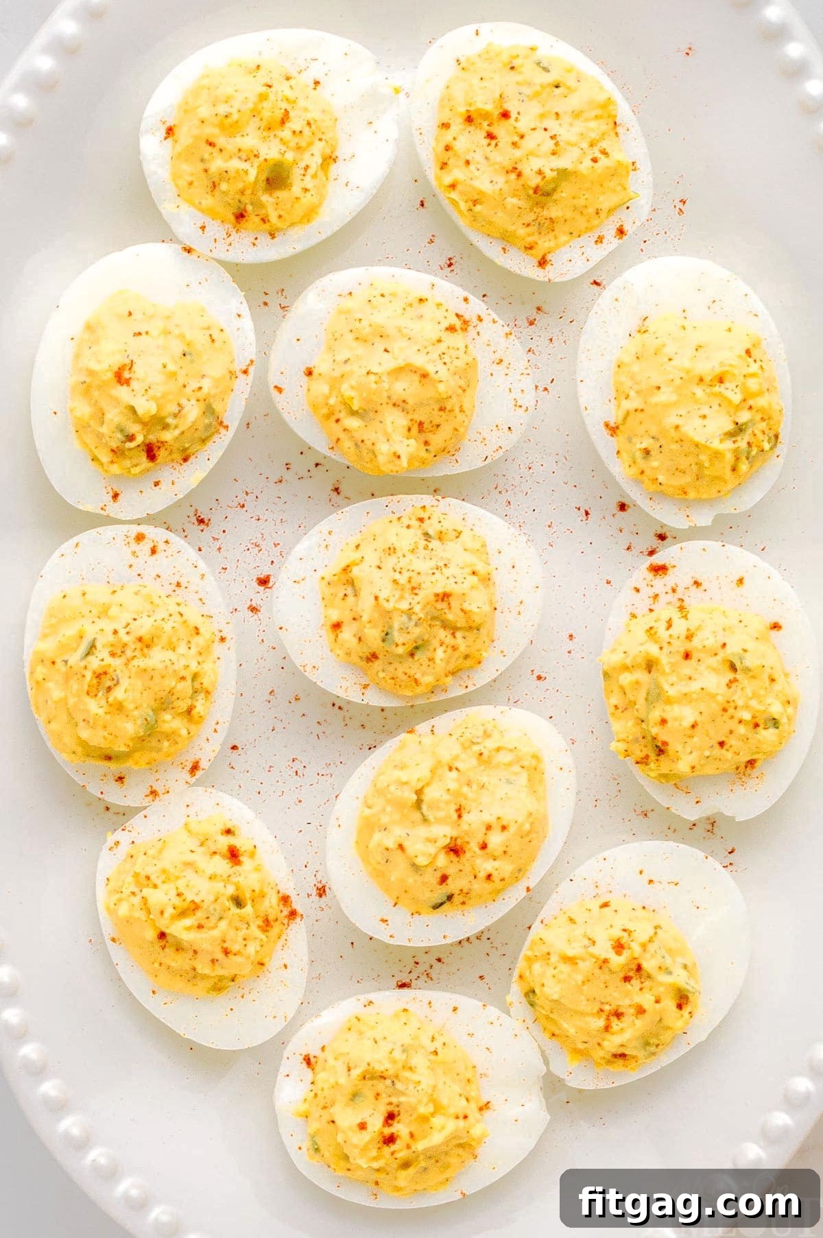 A detailed close-up of beautifully arranged deviled eggs on a white tray with a delicate beaded edge, each egg meticulously dusted with paprika for an inviting finish.
