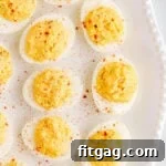 close up of deviled eggs on a white tray with a beaded edge dusted with paprika.