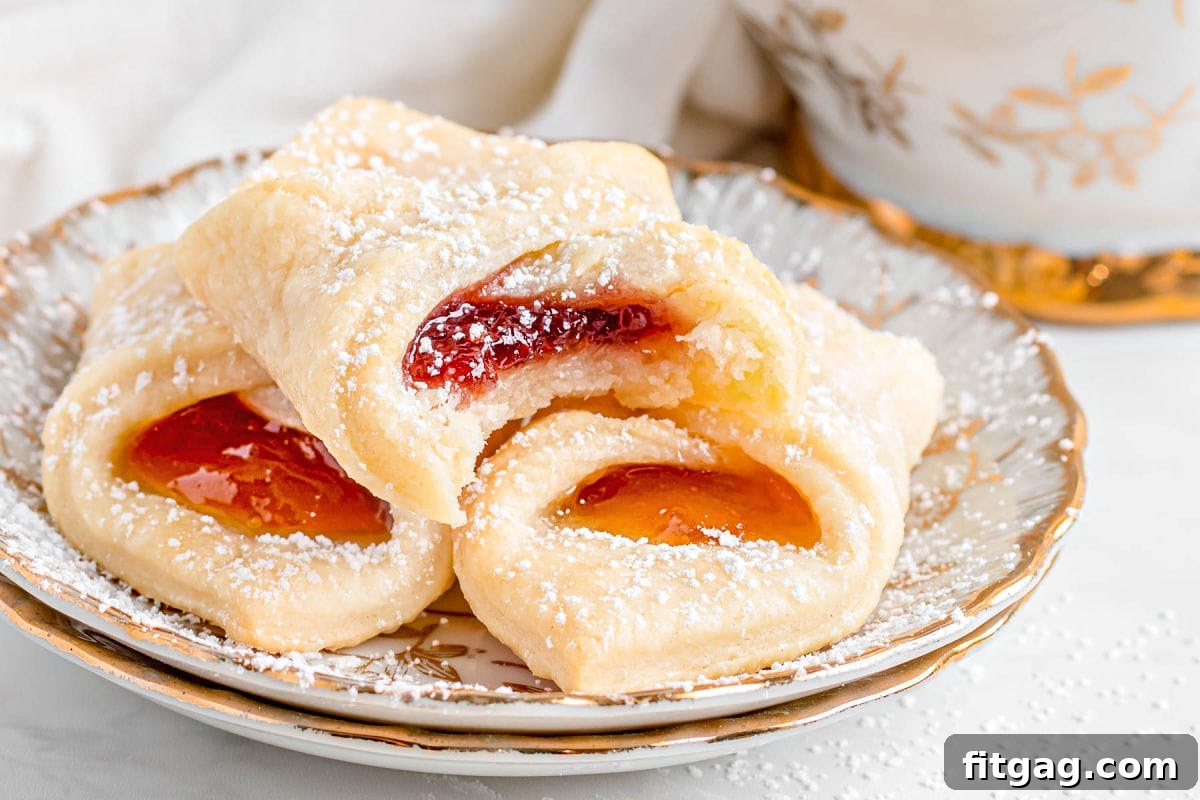 Three Kolaczki cookies on a small gold-rimmed plate, with one cookie having a bite taken out of it.