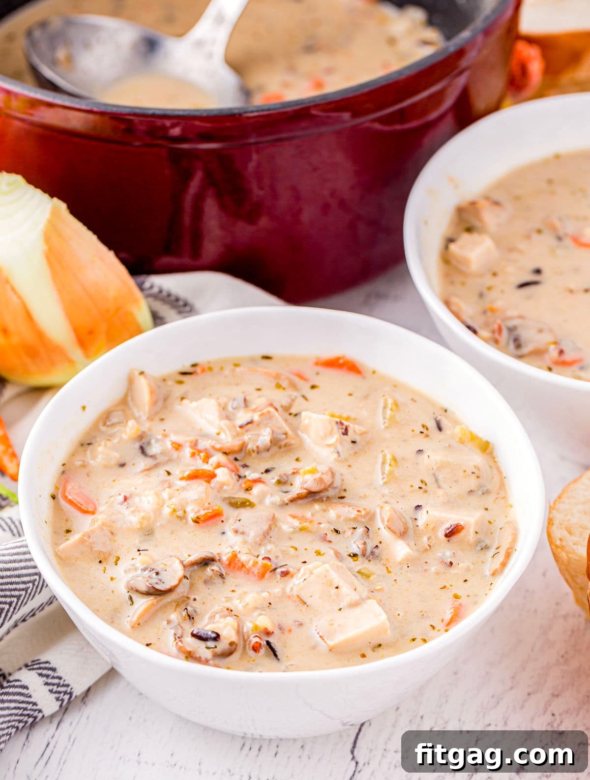 A white bowl of turkey and wild rice soup sits in front of a rustic Dutch oven, hinting at cozy warmth.