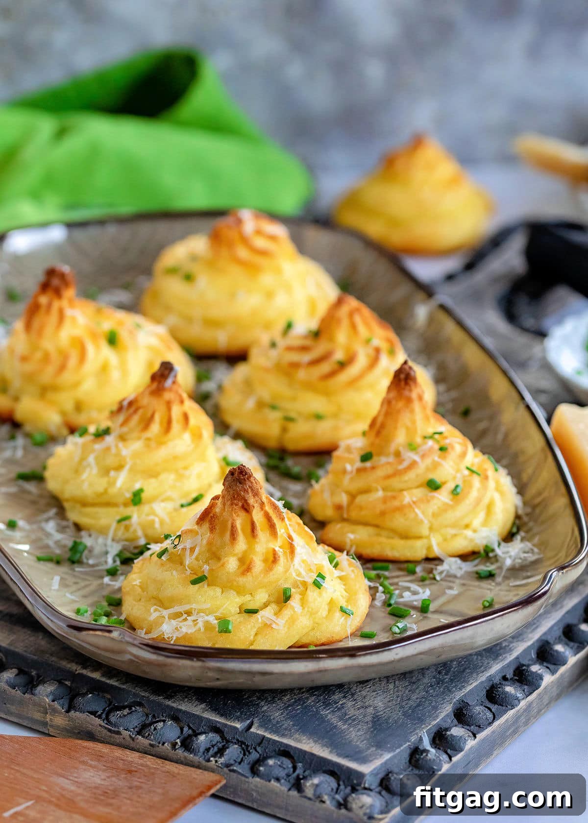 Large brown tray showcasing six golden-brown Duchess Potatoes, elegantly garnished with freshly grated Parmesan cheese and finely snipped chives.