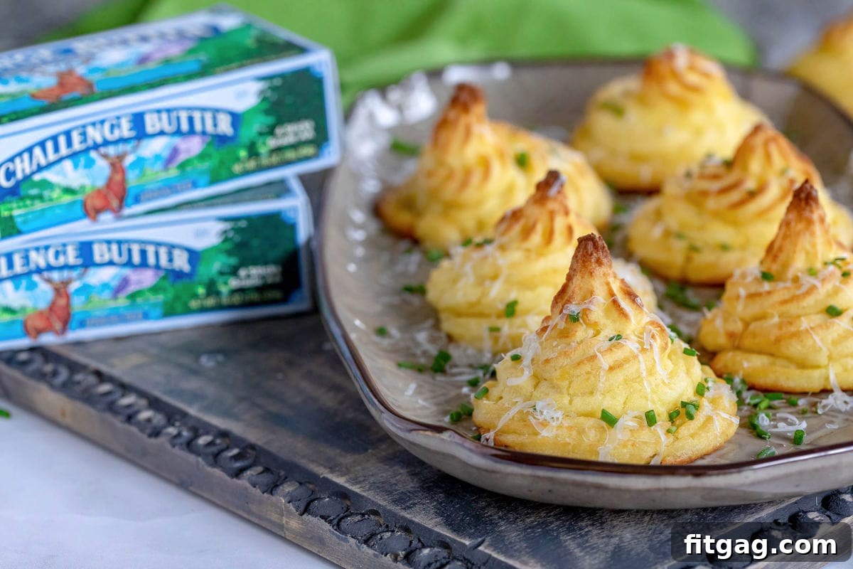 Six perfectly piped Duchess Potatoes arranged on a brown serving tray, with boxes of Challenge unsalted butter strategically placed to the left of the tray, highlighting a key ingredient.